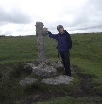 A woman standing next to an ancient stone cross on Dartmoor